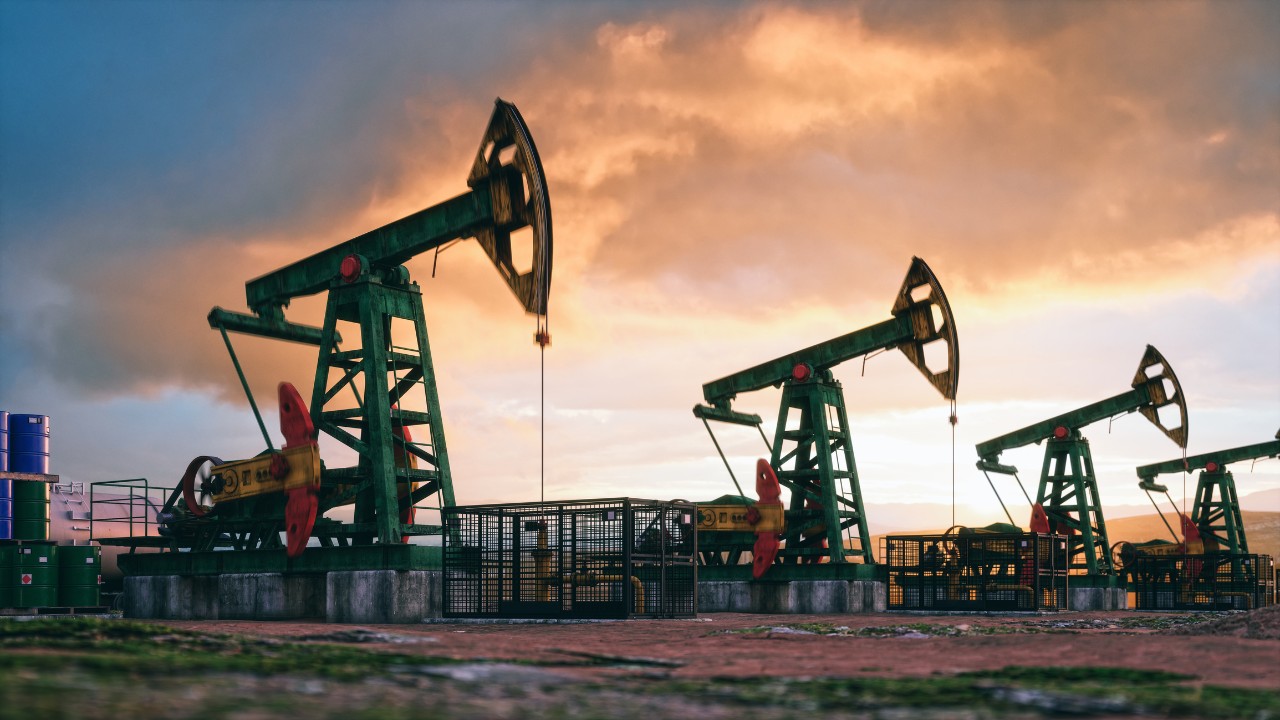 A row of four oil derricks in the evening light.