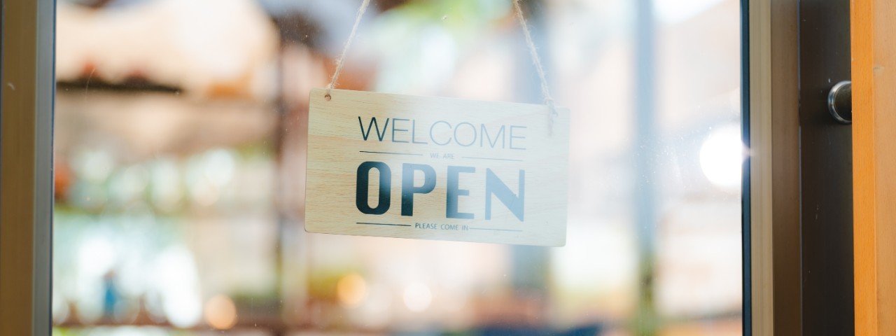 A sign on a store front reading, "Welcome, we are open, please come in."