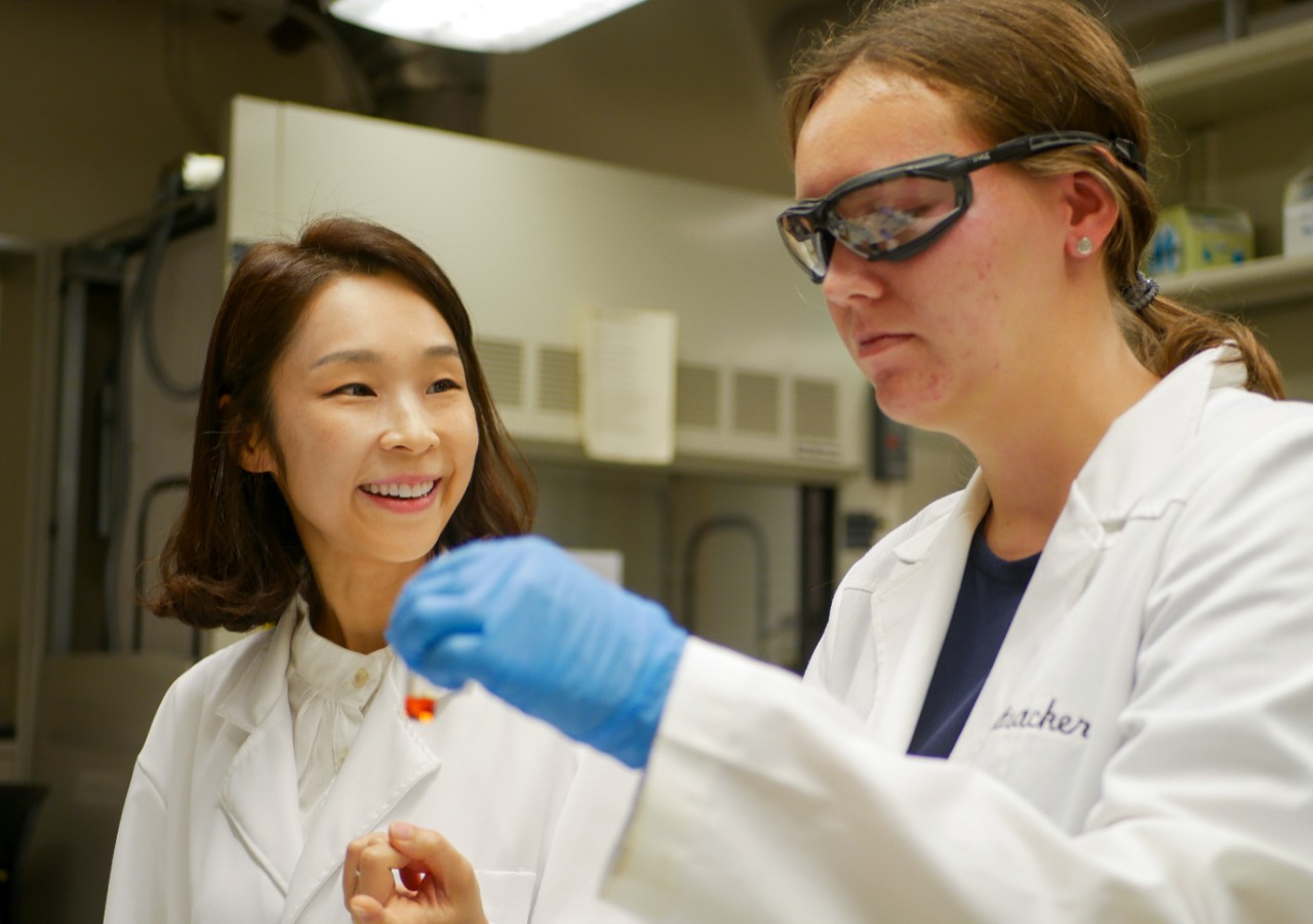 Yoonjee Park with a female student researcher in the lab looking at a vial of liquid